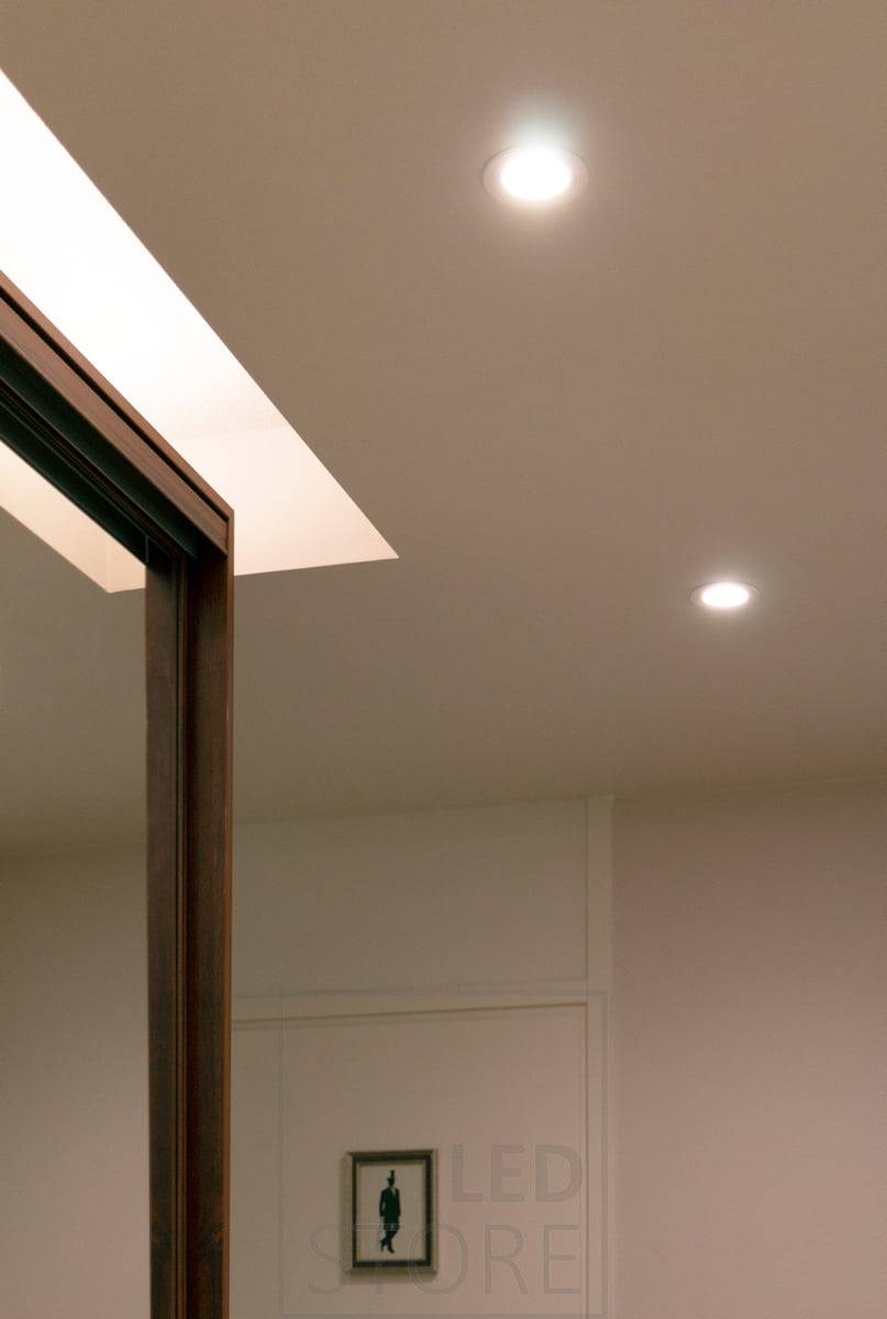Au-dessus de l'armoire à portes coulissantes dans le couloir, une bande LED en profilé de surface blanc et 7,2 W/m avec une bande LED CCT atmosphérique éclaire le plafond. LedStore.fi