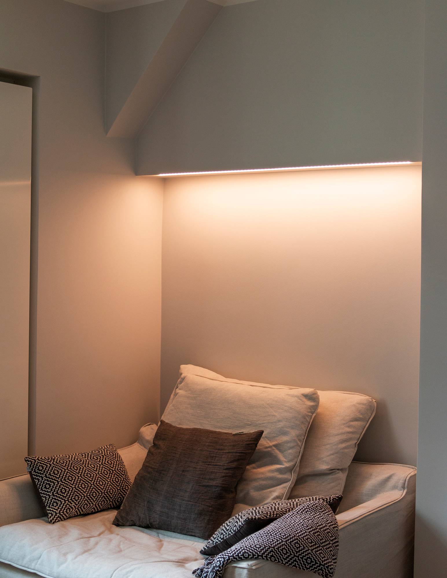Chambre à coucher avec éclairage d\'ambiance contrôlé par la température de couleur au-dessus du lit, bande LED montée sur le fond de l\'armoire dans une surface à profil bas. La lumière a une tonalité chaude dans l\'image. Ledstore.fi