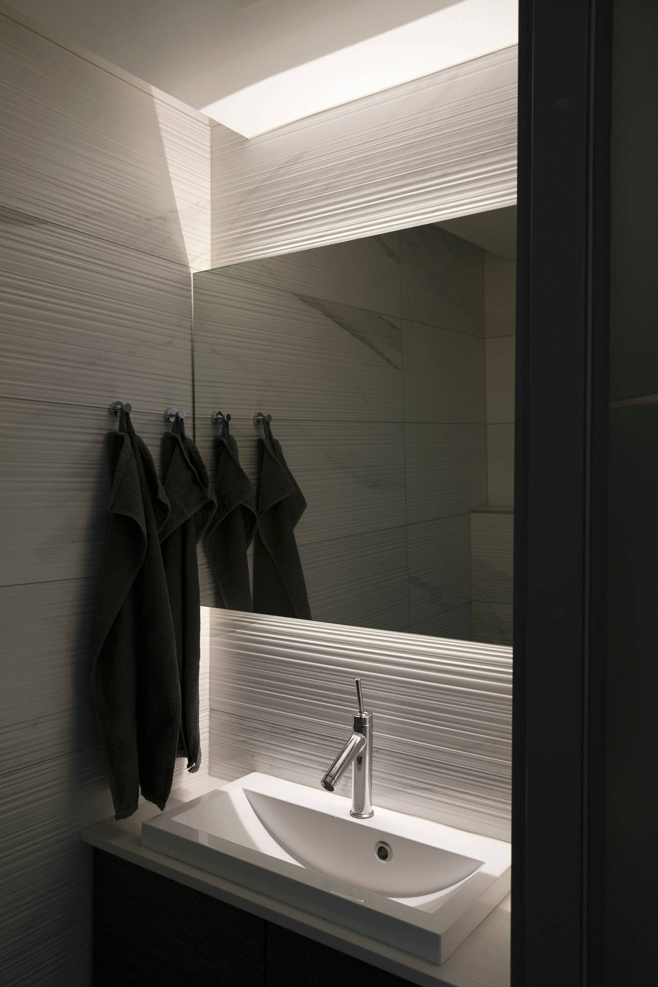 Les LED situées derrière le miroir mettent en valeur le carrelage texturé et le miroir. Ledstore.fi