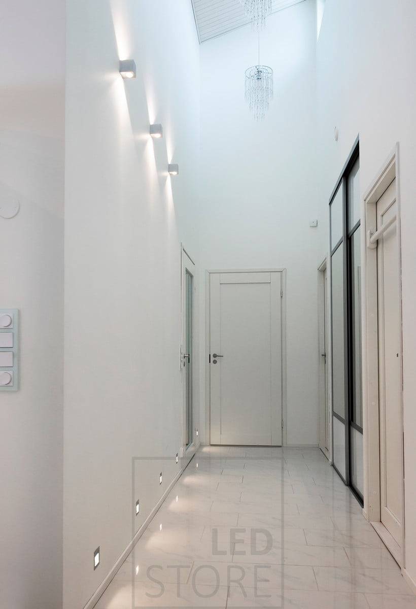 Les appliques encastrées IN-WALL créent une lumière indirecte dans le couloir au niveau du sol. Au-dessus, les appliques à leds CUBIC éclairent dans deux directions, soulignant la hauteur de l'espace. Ledstore.fi