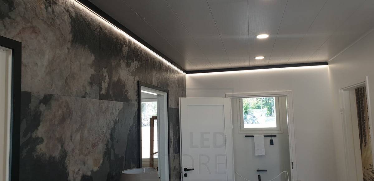 Un profilé mural noir décoratif et linéaire avec une bande lumineuse LED fournissant une lumière indirecte. Ledstore.fi