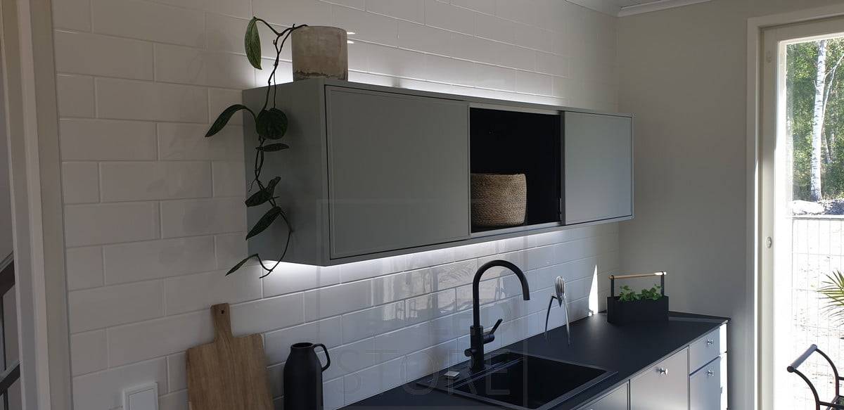 Des bandes LED éclairent le haut du placard et le plan de travail, créant un bel effet de lumière qui met en valeur la cuisine. Ledstore.fi