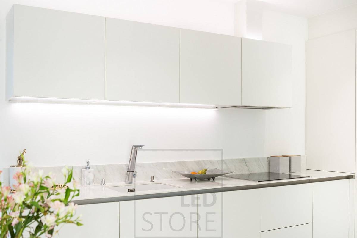 Des bandes LED sur le dessus des armoires et éclairant le plan de travail. La lumière neutre met en valeur les tons clairs de la cuisine blanche. Ledstore.fi