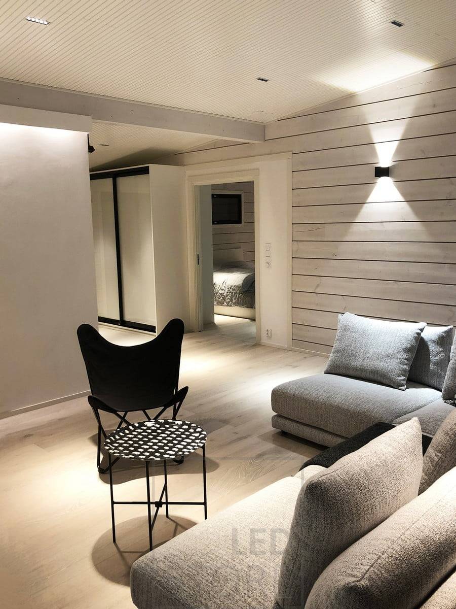 Un éclairage d'ambiance et polyvalent dans le salon. Une bande LED derrière le plafond éclaire indirectement l'espace, des spots LINJA au plafond et une applique FUNK au mur. Ledstore.fi