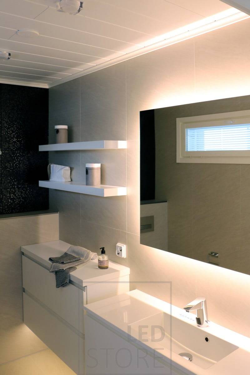 Éclairage doux et atmosphérique dans la salle de bains avec un miroir lumineux et une bande lumineuse LED sous le niveau du sol. Ledstore.fi