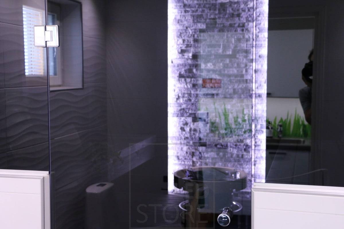 Mise en valeur des détails à l'aide d'une bande LED. Des bandes de LED sont disposées verticalement de part et d'autre du mur, mettant en valeur le beau mur de pierre derrière le poêle. Ledstore.fi