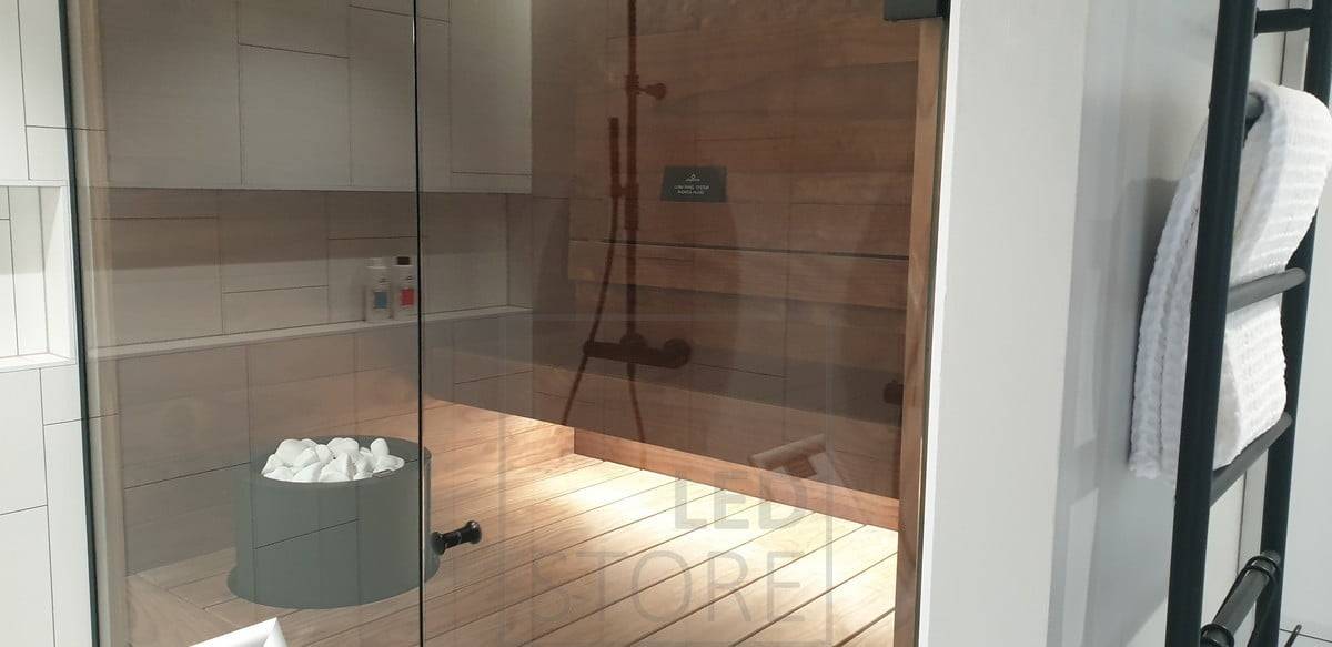 Un ruban de diodes électroluminescentes placé sous la condensation éclaire le sauna d'une lumière indirecte. L'éclairage des toilettes se prolonge dans le sauna grâce à la paroi en verre. Ledstore.fi