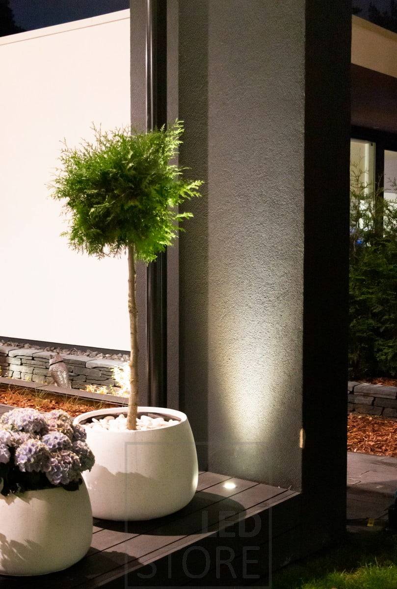 Un spot éclairant vers le haut, encastré dans une terrasse, utilise le mur comme surface réfléchissante. La lumière met également en valeur la plante qui se trouve devant. Ledstore.fi