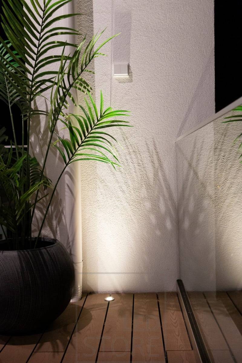 Un projecteur à éclairage vers le haut encastré dans la terrasse utilise le mur comme surface réfléchissante pour éclairer la pièce avec une lumière atmosphérique du bas vers le haut. Ledstore.fi