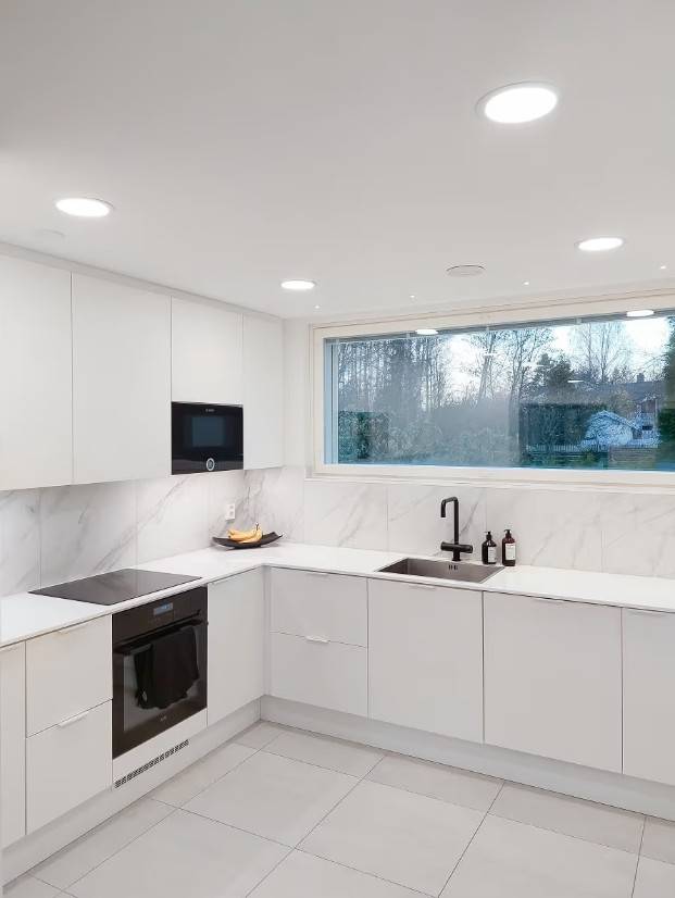 Des panneaux lumineux au plafond de la cuisine, des bandes lumineuses LED sous les armoires et de petits spots d'accentuation alignés devant la fenêtre.  