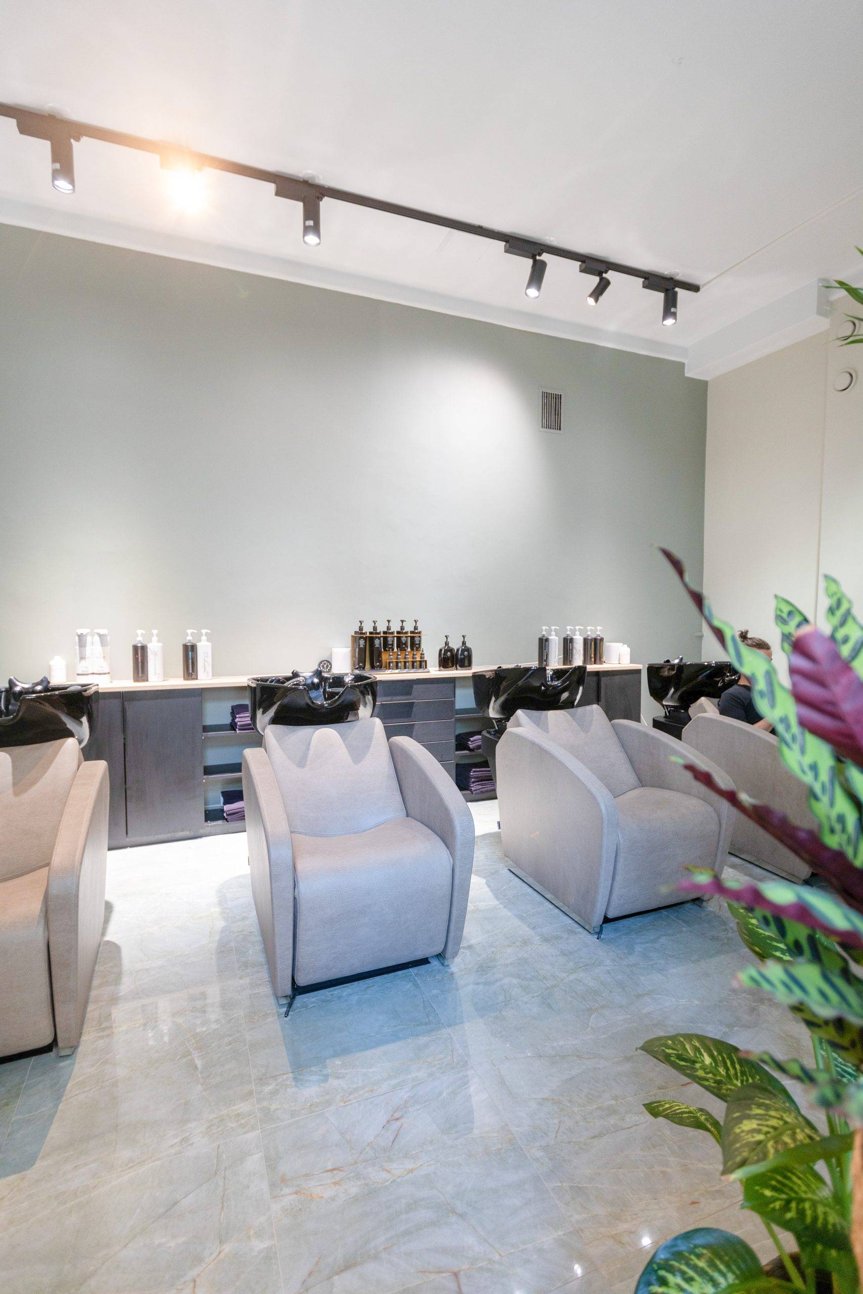 Salle de bain d'un salon de coiffure avec des surfaces claires et des rails triphasés noirs montés au plafond, ainsi que des pots de rails noirs FOKUS.