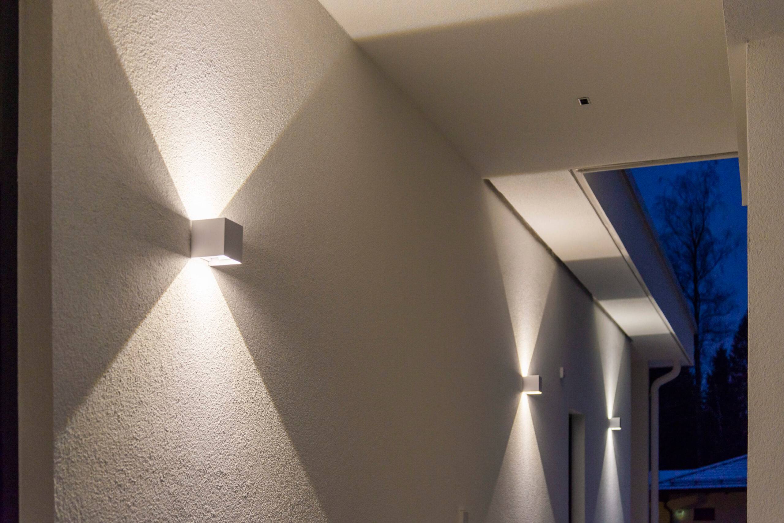 Les appliques murales cubiques à LED blanches éclairent à la fois vers le haut et vers le bas, créant un motif lumineux net sur le mur.