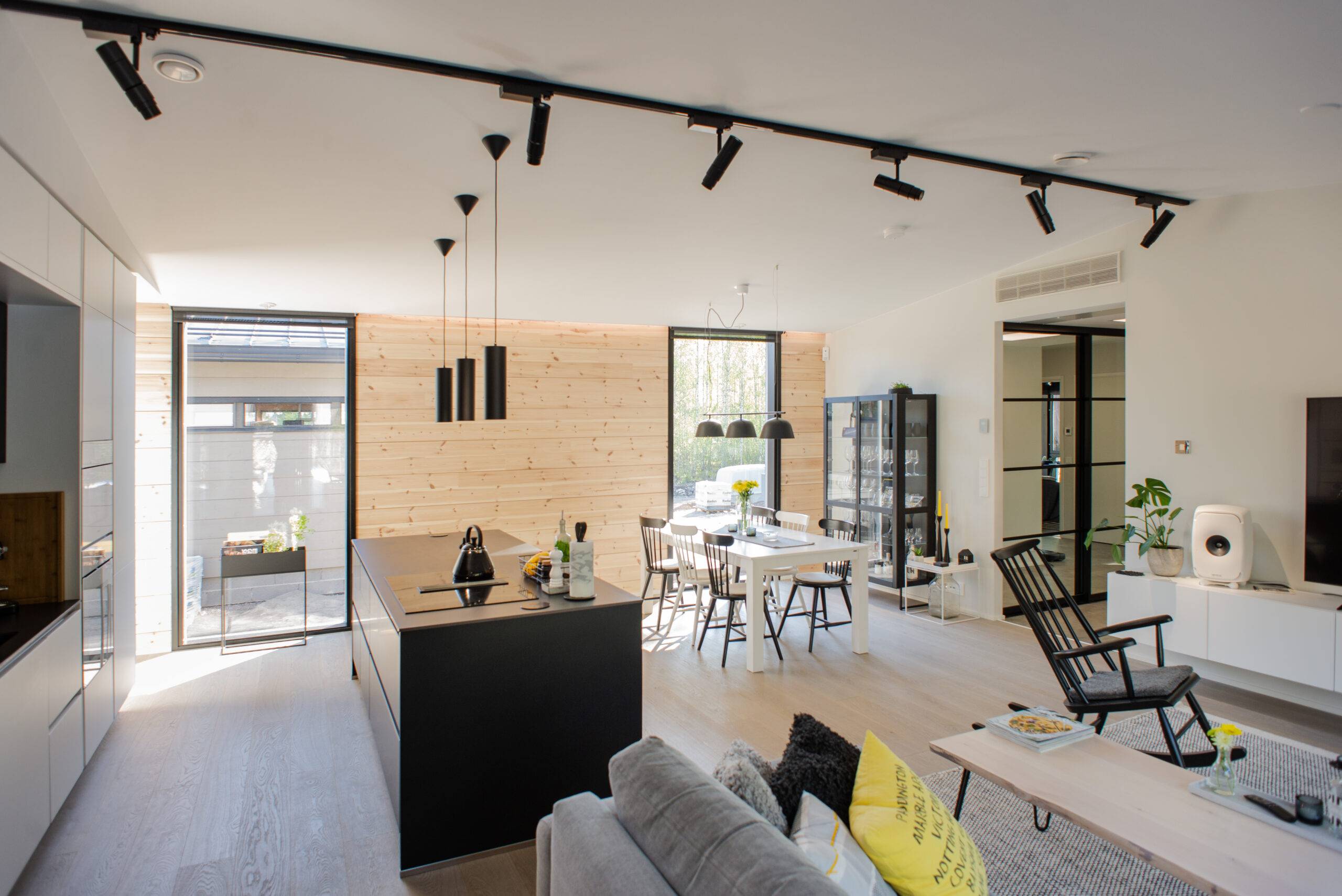 Cuisine et salon ouverts modernes avec des détails en bois et des meubles noirs pour un look élégant. L'éclairage intérieur de haute qualité de LedStore.fi crée une atmosphère agréable et les grandes fenêtres laissent entrer la lumière naturelle. 