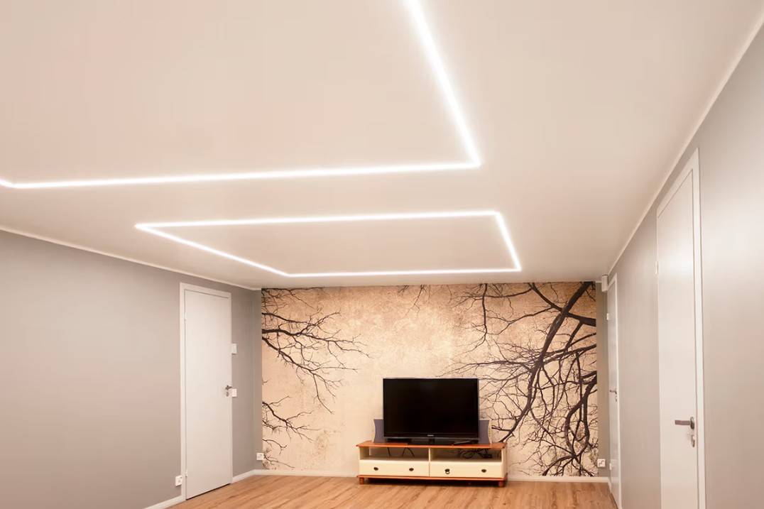 Un salon minimaliste dans une maison familiale à Kaitamäki, Espoo, où les plafonniers LED de LedStore.fi créent un système d'éclairage élégant. Le salon comporte une table de télévision et une peinture murale remarquable, accentuée par un éclairage LED de haute qualité.