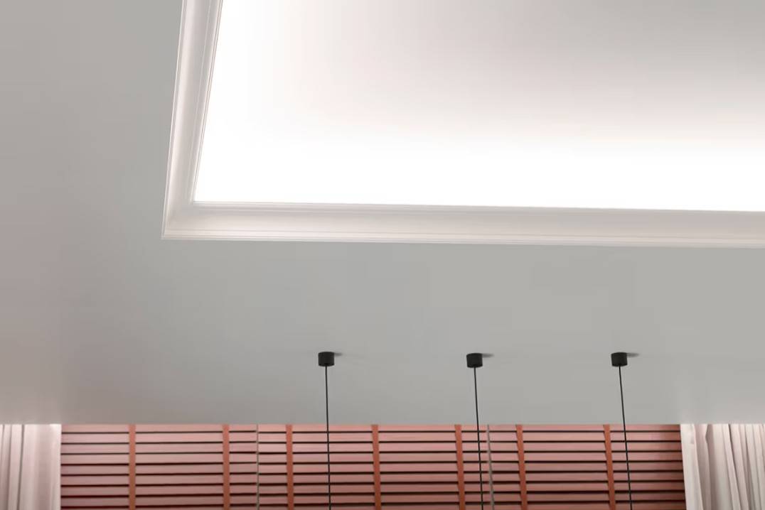 Un ensemble d'éclairage fonctionnel pour le salon. La bande lumineuse LED sur l'étagère du plafonnier éclaire vers le plafond et vers le bas en direction des rideaux.