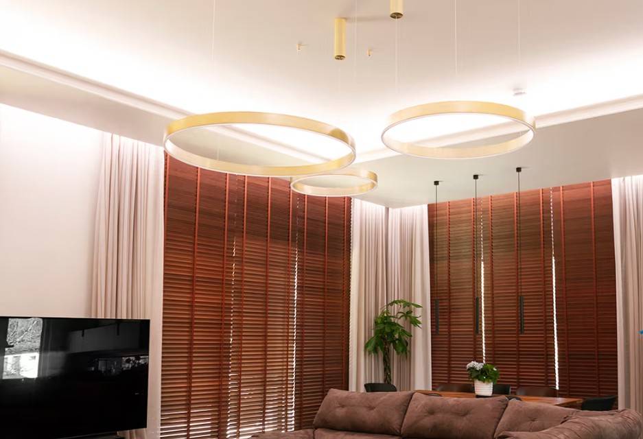 Ce salon familial moderne de Kaitamäki, à Espoo, est doté d'un superbe éclairage LedStore.fi : de grands anneaux lumineux dorés créent une atmosphère luxueuse, accompagnés de stores bruns assortis et d'un canapé confortable. Le tout est complété par une télévision élégante et une végétation luxuriante - c'est le genre d'éclairage qui donne à votre maison un aspect confortable et impressionnant !