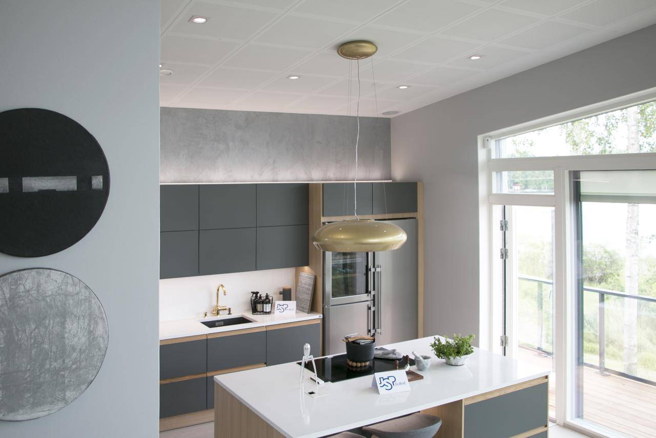 Cuisine moderne avec des armoires vert foncé, un îlot blanc, des lampes suspendues dorées, des appareils électroménagers ; art mural LED qui met en valeur la lumière naturelle des grandes fenêtres.