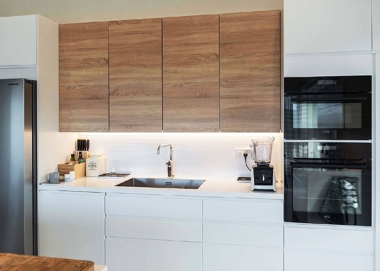 Cuisine moderne avec armoires supérieures en bois, plans de travail blancs éclairés par LED, évier en acier inoxydable avec robinet chromé, double four et appareils électroménagers de comptoir.