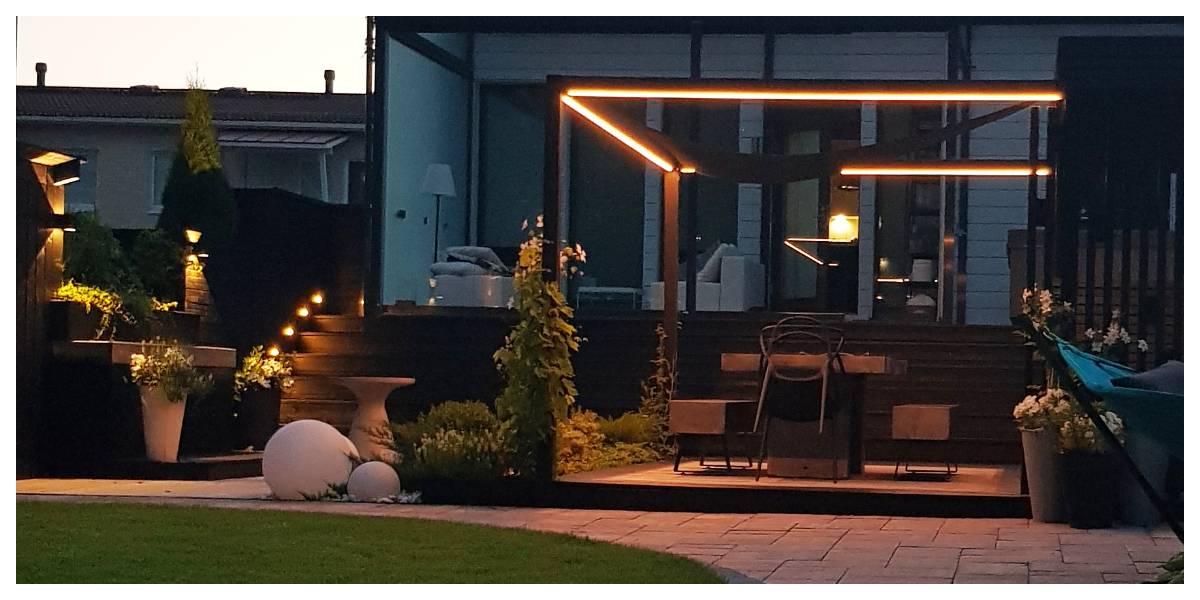 Terrasse moderne avec pergola et éclairage d'ambiance LED. Marches en bois et plantes en pot d'ambiance. Situé dans la cour d'une maison moderne, l'ensemble offre un cadre parfait pour les soirées avec l'éclairage LED de haute qualité de LedStore.fi.  
