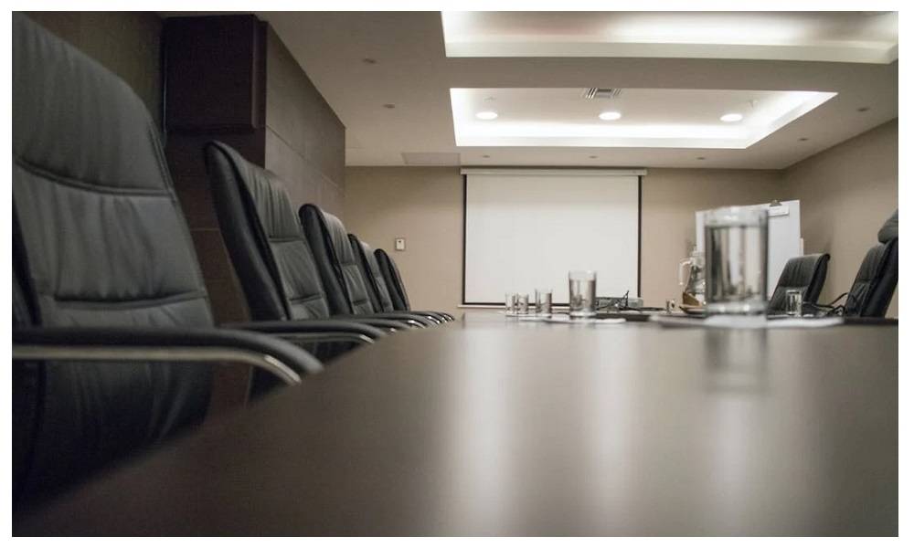 Salle de conférence avec une grande table sombre et des chaises. Plusieurs panneaux et spots lumineux sont installés au plafond.  