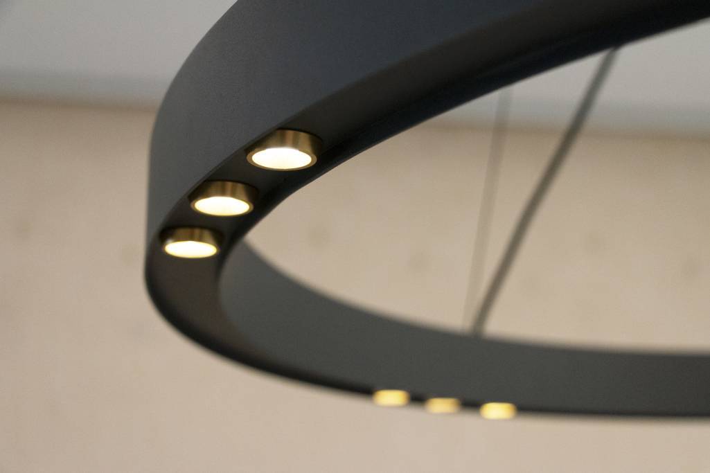 Gros plan sur un lustre rond moderne noir mat avec des lumières LED encastrées qui créent une douce lueur sur un fond flou pour une atmosphère élégante.