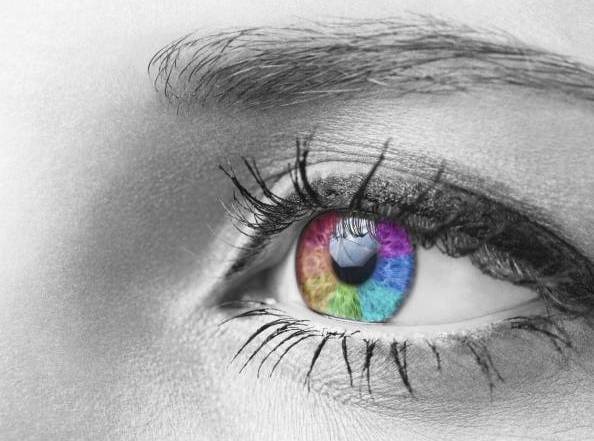 Gros plan d'un œil gris dont l'iris, semblable à celui d'une DEL, est irisé de couleurs vives : rouge, bleu, vert, violet ; contraste frappant avec la peau et les cils monochromes.