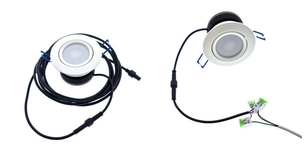 Deux downlights LED ronds avec des cadres blancs sont attachés à de longs fils noirs. Les lampes sont équipées de connecteurs à l'extrémité des fils. L'un des fils est torsadé, tandis que l'autre se prolonge et se connecte aux connecteurs en ligne verts, mettant en évidence sa propre intégration élégante des LED.