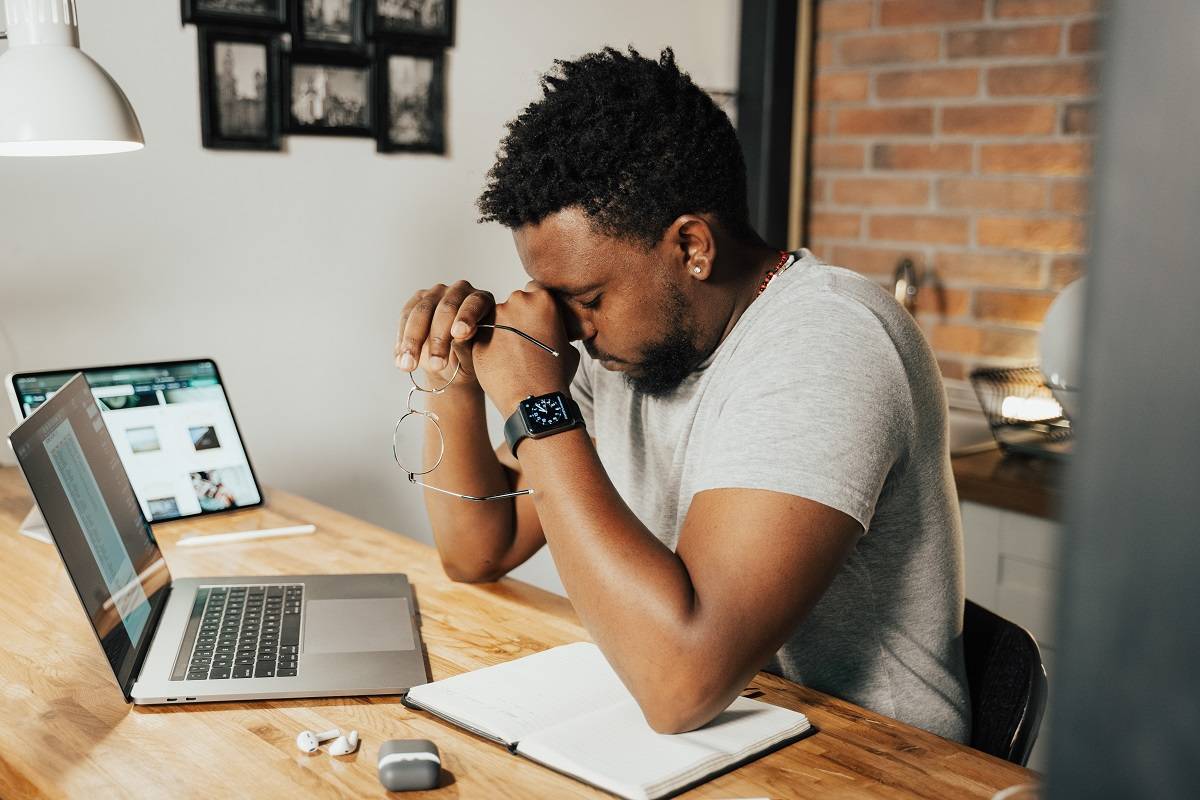 L'homme a enlevé ses lunettes et appuie sa tête sur ses mains à son bureau.