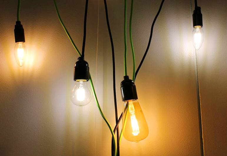 Les fils noirs et verts de quatre lampes LED élégantes sont suspendus contre un mur clair, pour un intérieur moderne.