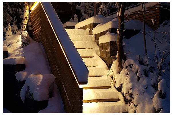 Escalier enneigé à la tombée de la nuit, avec une lumière chaude éclairant l'escalier depuis la balustrade.  