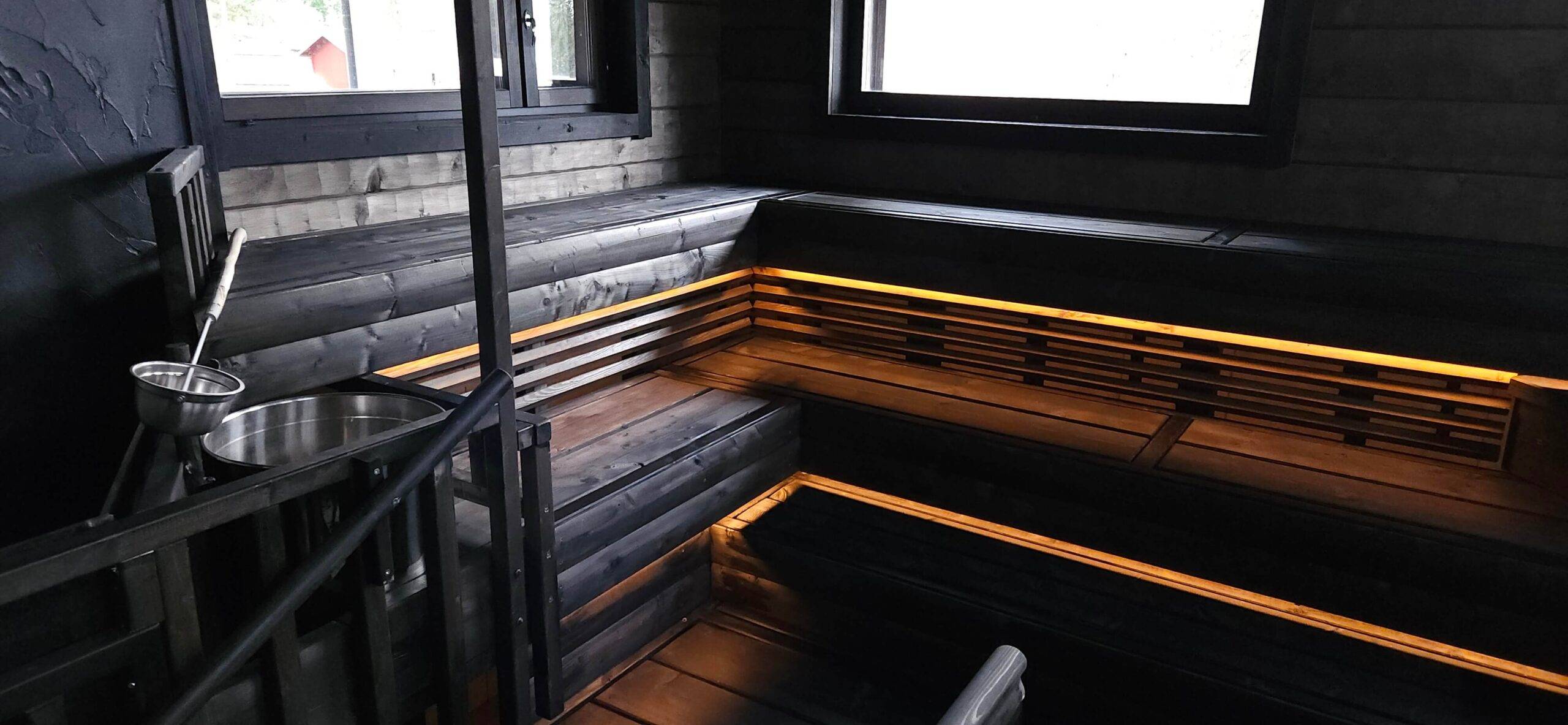 au bas du plafond du sauna en bois foncé, des bandes lumineuses LED jaunâtres et chaudes ont été installées pour éclairer vers le bas.