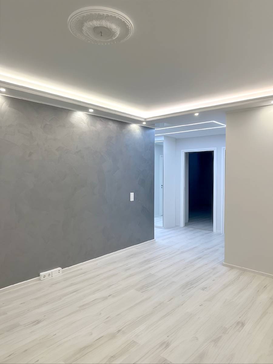Une structure de plafond avec un faux plafond à partir des bords de la pièce, avec un éclairage indirect par bandes LED et des spots vers le bas.
